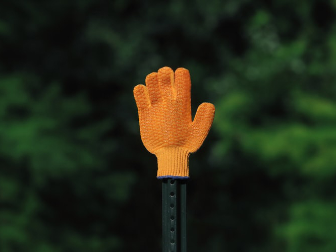 orange glove gesturing stop with greenery background